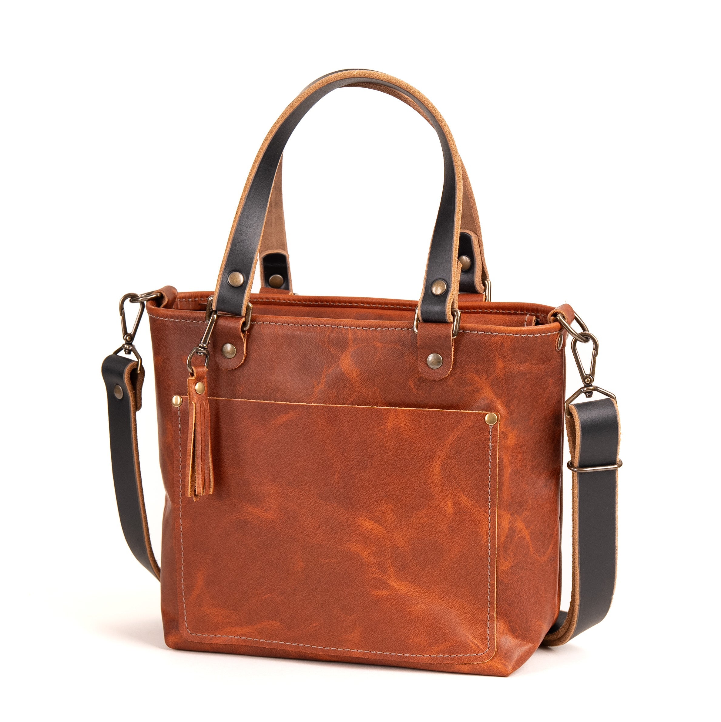 A brown leather handbag with dark brown handles and shoulder strap, featuring a front pocket with a tassel detail, set against a plain white background.