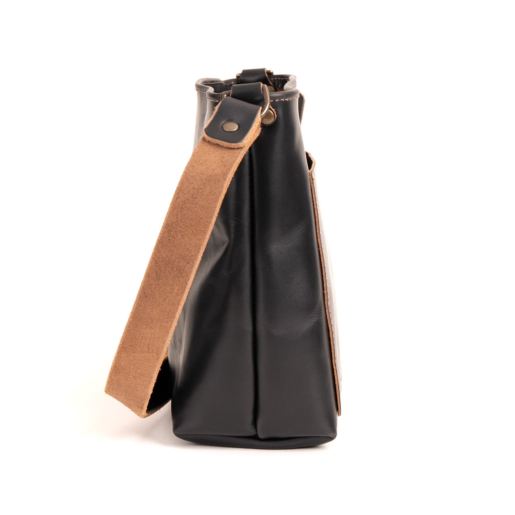 A black leather tote bag with a wide tan suede-like shoulder strap, shown from a side profile view against a plain white background.